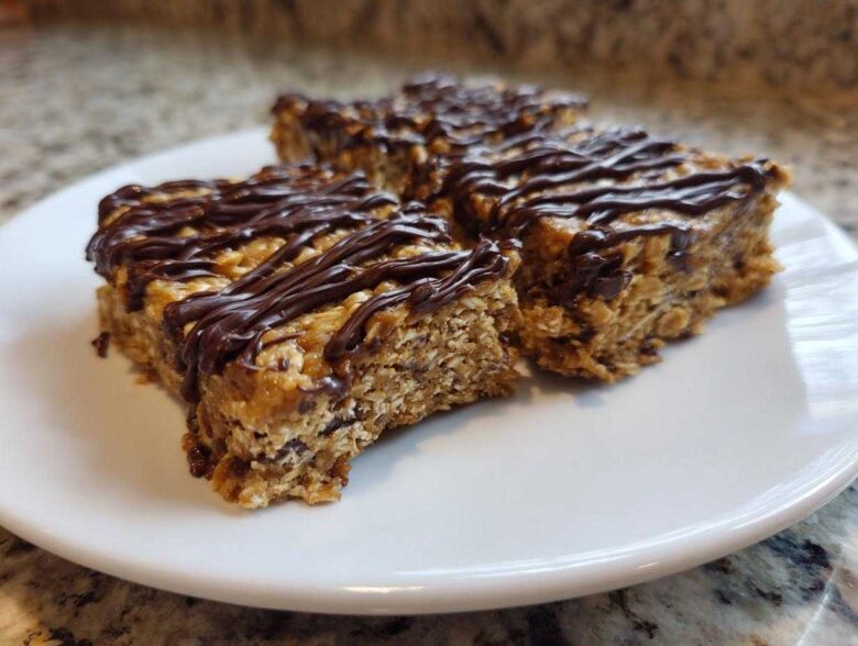 Three homemade protein bars with oats and a rich chocolate drizzle served on a white plate.