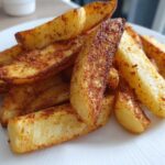 A close-up of golden brown, seasoned air fryer potato wedges piled high on a white plate.