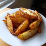 A close-up of golden brown, seasoned air fryer potato wedges piled high on a white plate.
