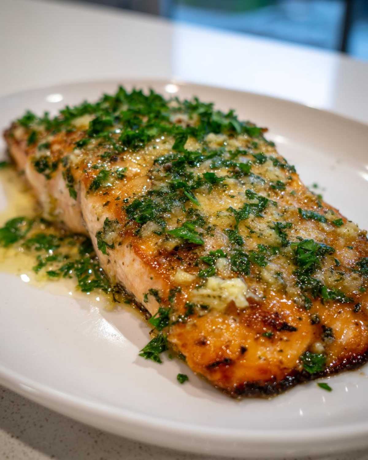 Close-up of a glistening fillet of air fryer salmon topped with melted butter, garlic, and fresh chopped parsley.
