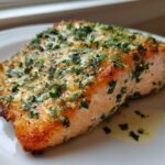 Close-up of a flaky, golden-brown piece of air fryer salmon topped with melted butter and fresh parsley.