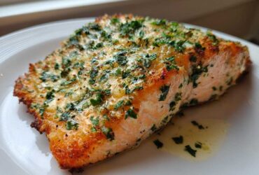 Close-up of a flaky, golden-brown piece of air fryer salmon topped with melted butter and fresh parsley.