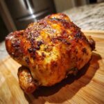 Close-up of a perfectly cooked, crispy-skinned air fryer whole chicken resting on a wooden cutting board.