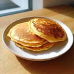 A stack of three golden brown almond flour pancakes resting on a speckled white plate.