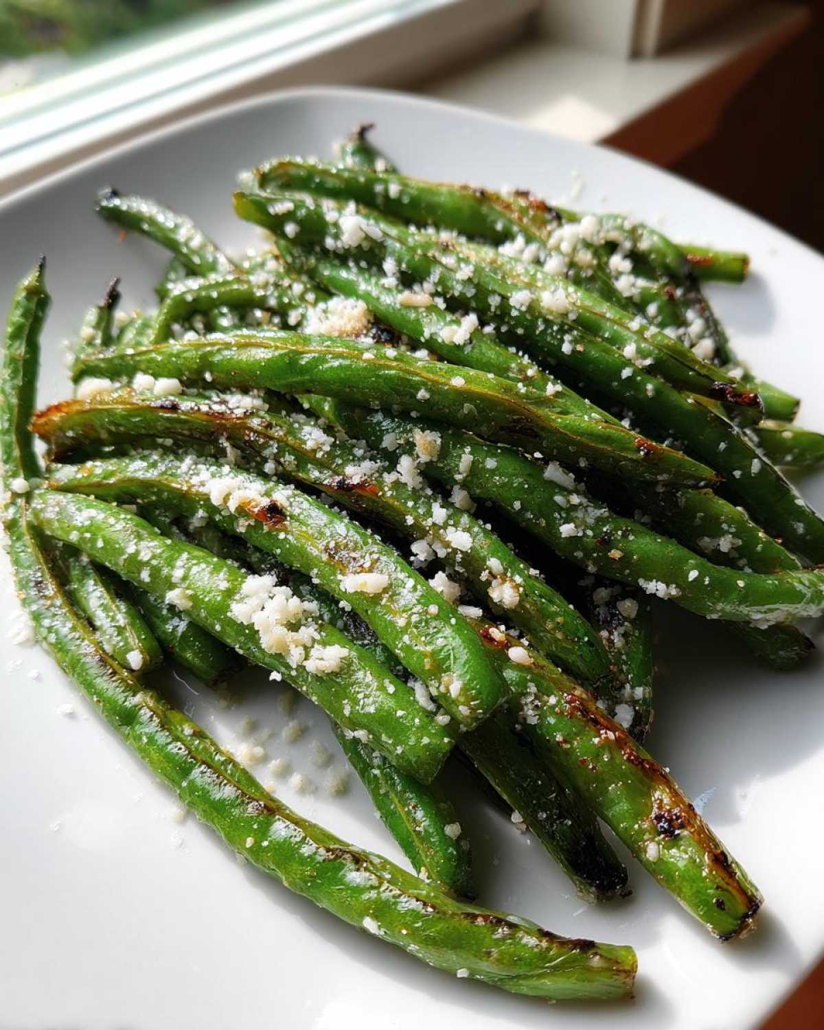 Close-up of bright green beans roasted until slightly charred and topped with grated Parmesan cheese.