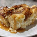Close-up of a moist slice of bread pudding topped generously with rich vanilla sauce.