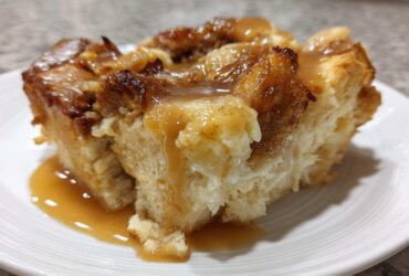 Close-up of a moist slice of bread pudding topped generously with rich vanilla sauce.