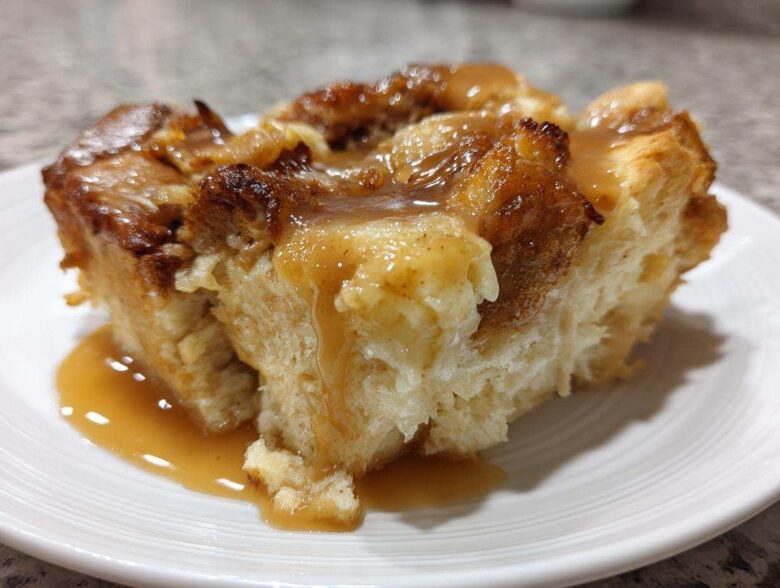 Close-up of a moist slice of bread pudding topped generously with rich vanilla sauce.
