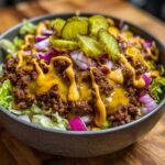 A close-up of a delicious cheeseburger bowl featuring seasoned ground beef, melted cheese, pickles, and red onion over lettuce.