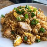 Close-up of savory chicken fried rice mixed with scrambled egg pieces and topped with fresh green onions.