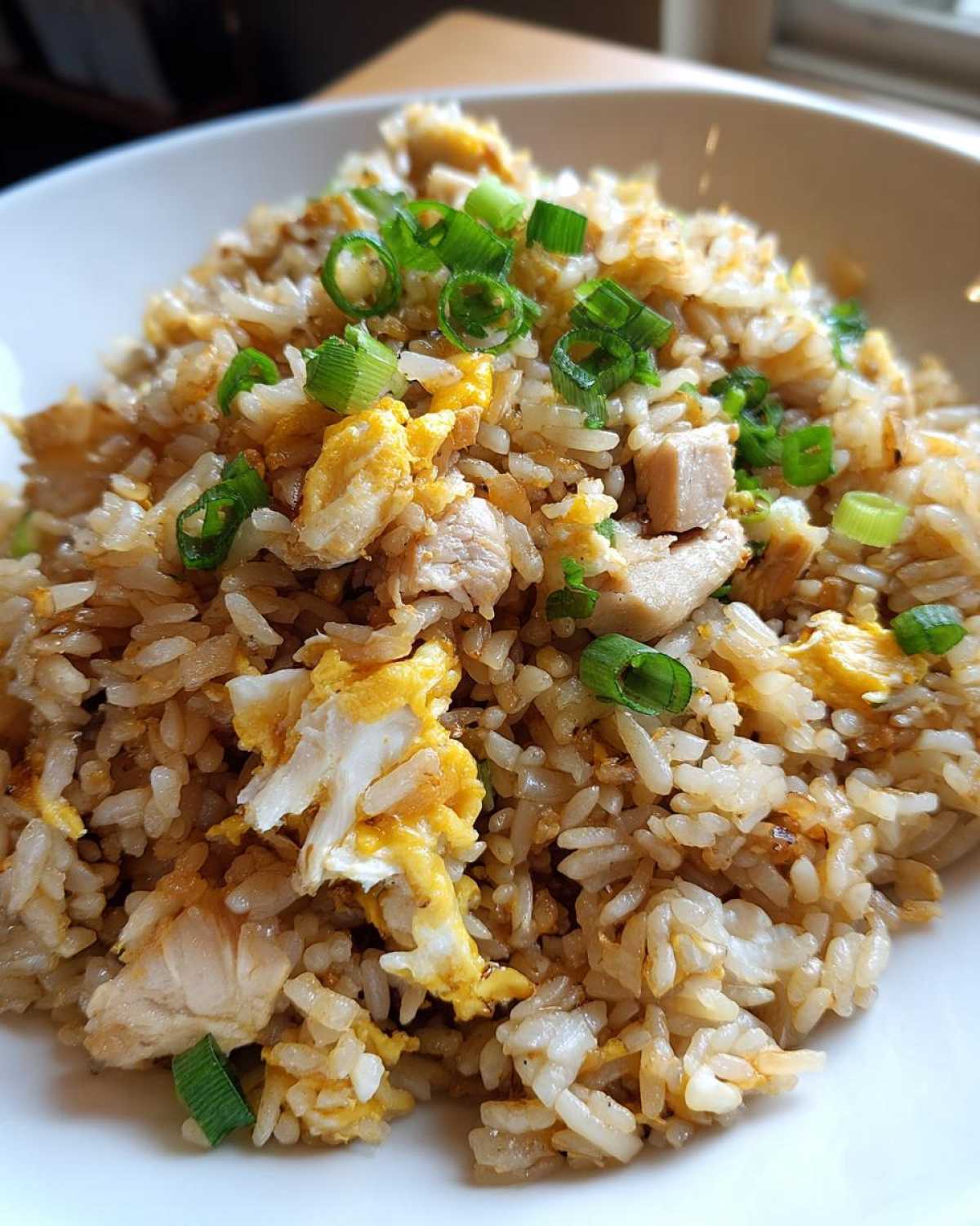 A close-up serving of amazing chicken fried rice featuring visible pieces of chicken, scrambled egg, and topped with fresh green onions.