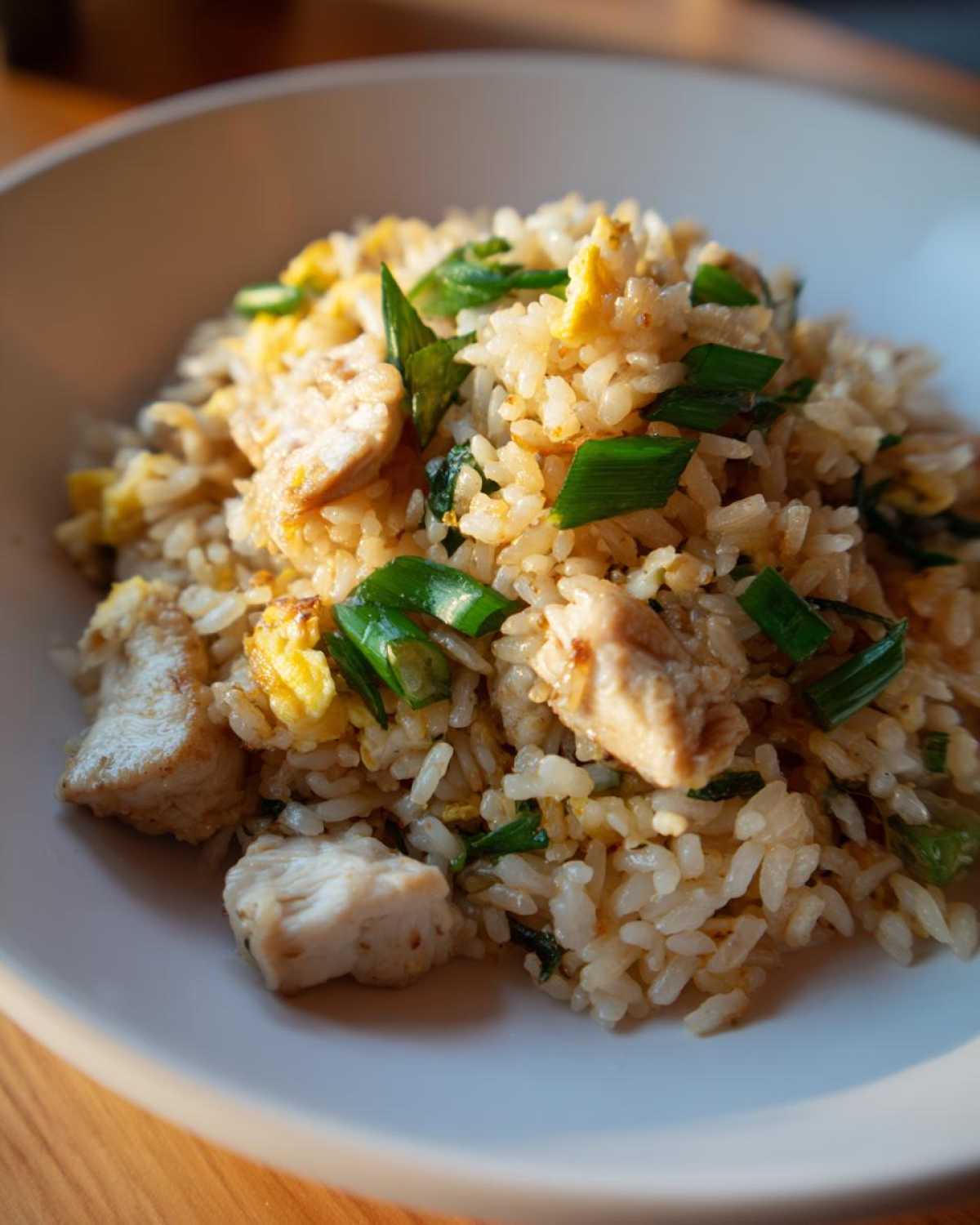 A close-up, appetizing shot of amazing chicken fried rice garnished generously with chopped green onions and visible chunks of white meat chicken.
