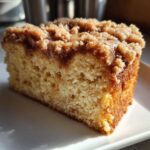 Close-up of a moist slice of coffee cake featuring a thick, crumbly cinnamon streusel topping.