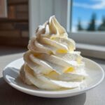 A tall, perfectly piped swirl of rich cream cheese frosting sitting on a small white plate.