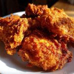 Close-up of several pieces of perfectly golden brown, crispy fried chicken piled on a white plate.