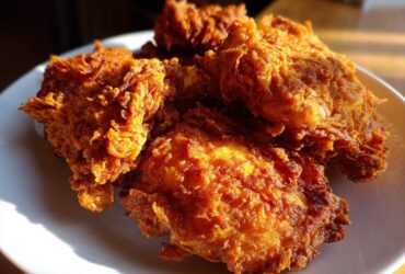 Close-up of several pieces of perfectly golden brown, crispy fried chicken piled on a white plate.