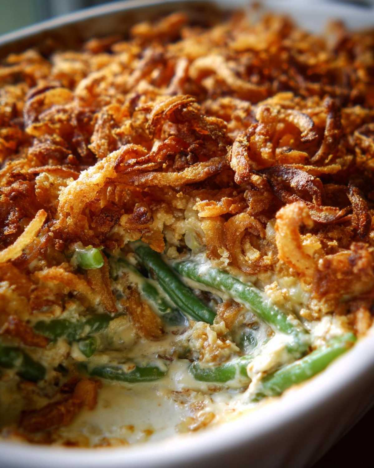 A close-up view showing a scoop taken out of a creamy green bean casserole topped with crispy fried onions.