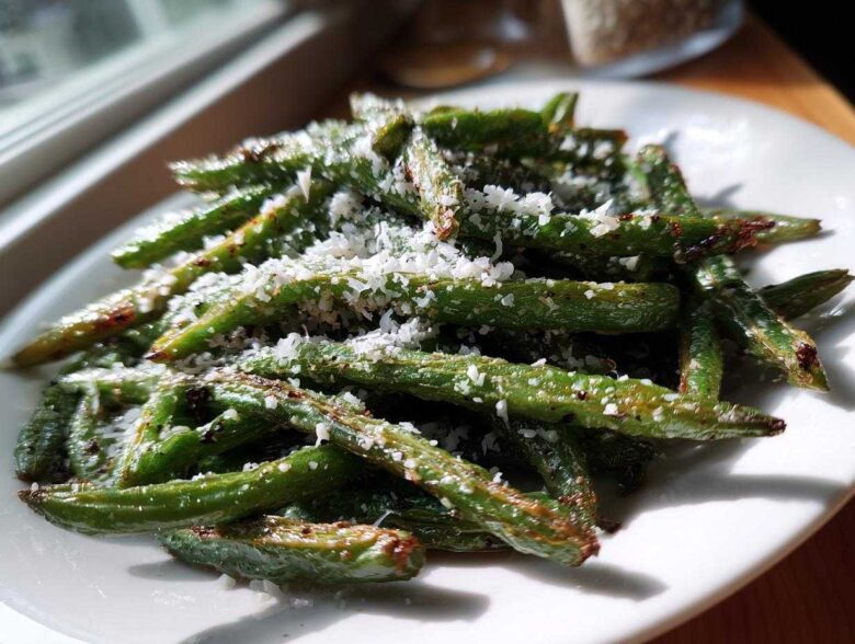 Close-up of roasted green beans topped with freshly grated Parmesan cheese, ready to serve.