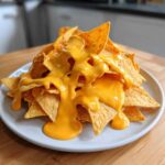 A pile of tortilla chips smothered in thick, bright orange nacho cheese sauce, ready to eat.