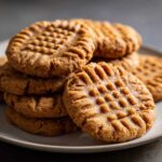 A close-up stack of freshly baked peanut butter cookies showing the classic crisscross fork pattern.