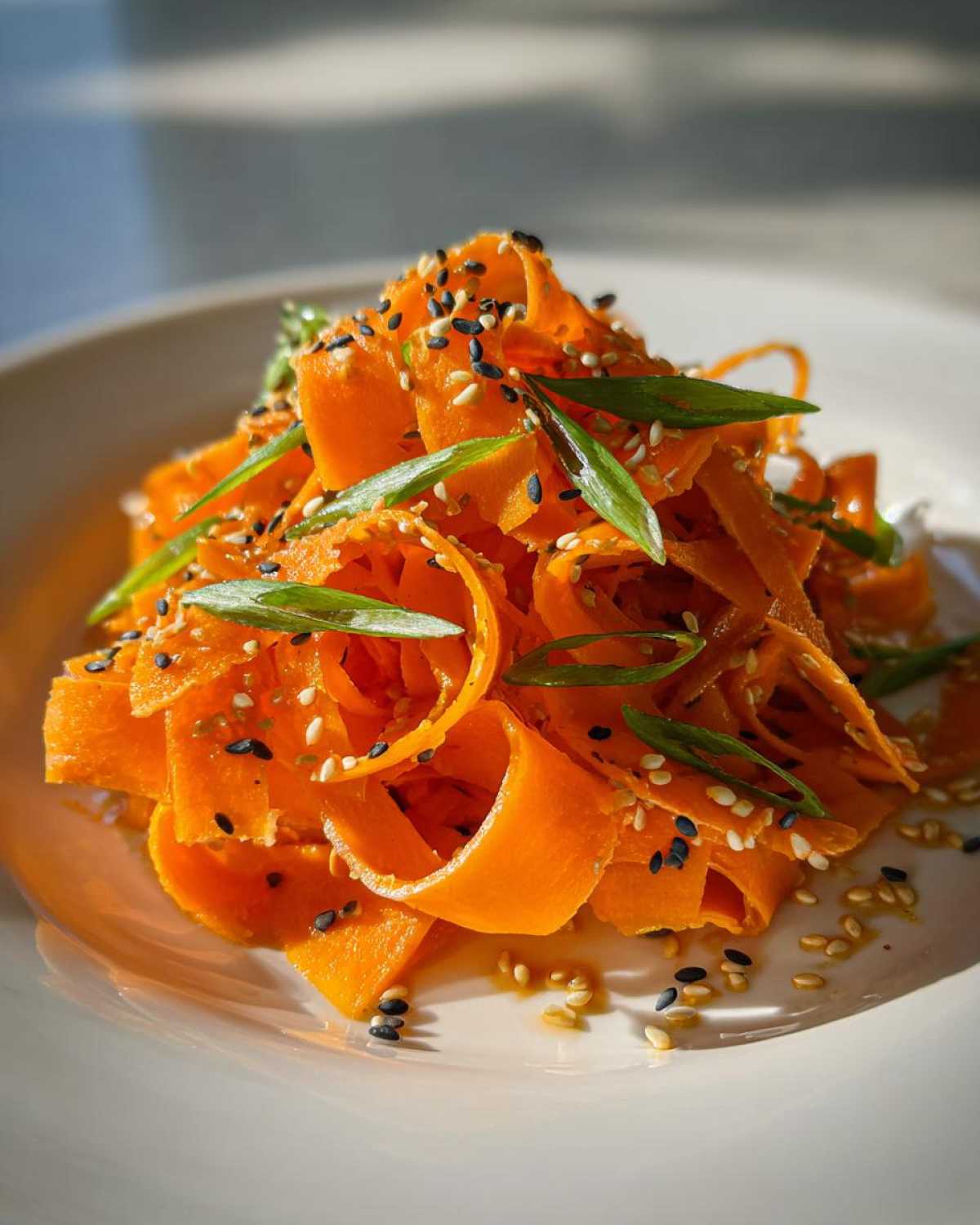Close-up of a vibrant raw carrot salad made with shaved carrot ribbons, topped with black and white sesame seeds.