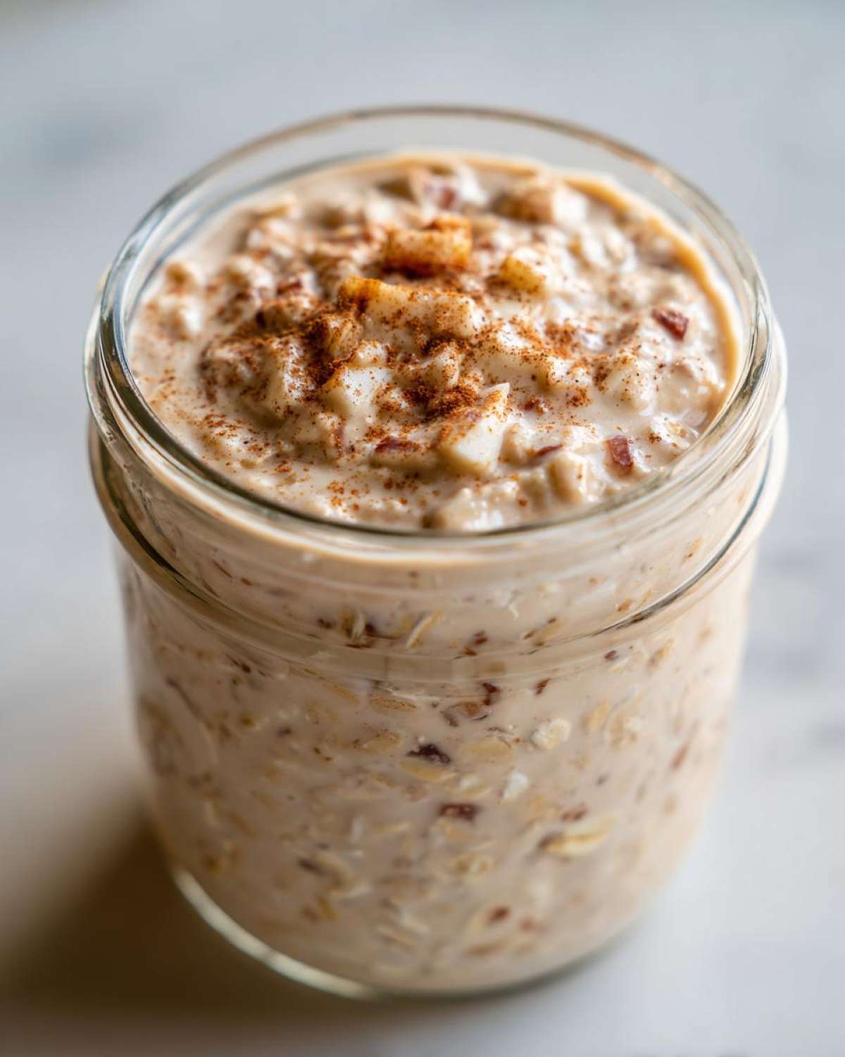 Close-up of apple cinnamon overnight oats in a glass jar, topped with diced apples and cinnamon.