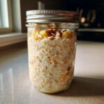 A glass jar filled with creamy apple cinnamon overnight oats, topped with diced apples and nuts.