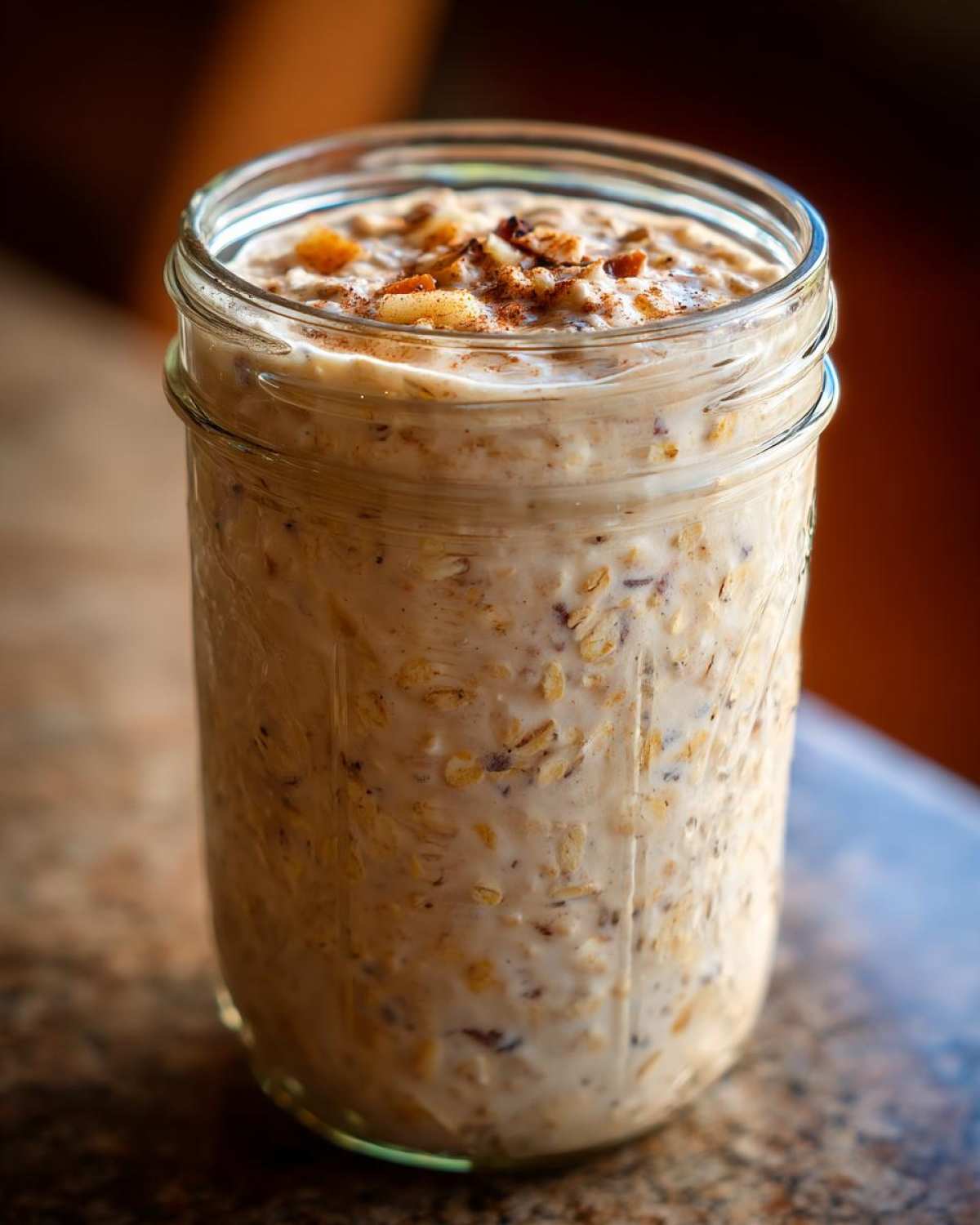 Close-up of apple cinnamon overnight oats prepared in a glass mason jar, topped with nuts and cinnamon.