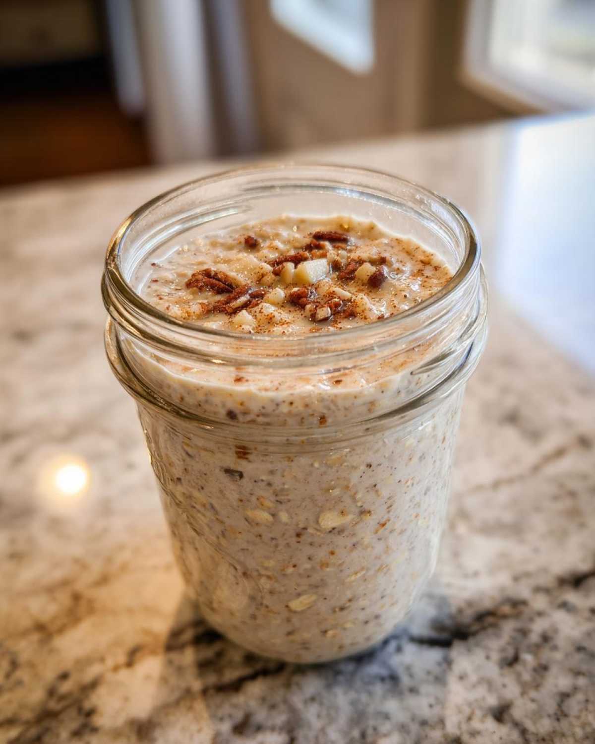 Close-up of apple cinnamon overnight oats in a glass jar, topped with pecans and cinnamon.