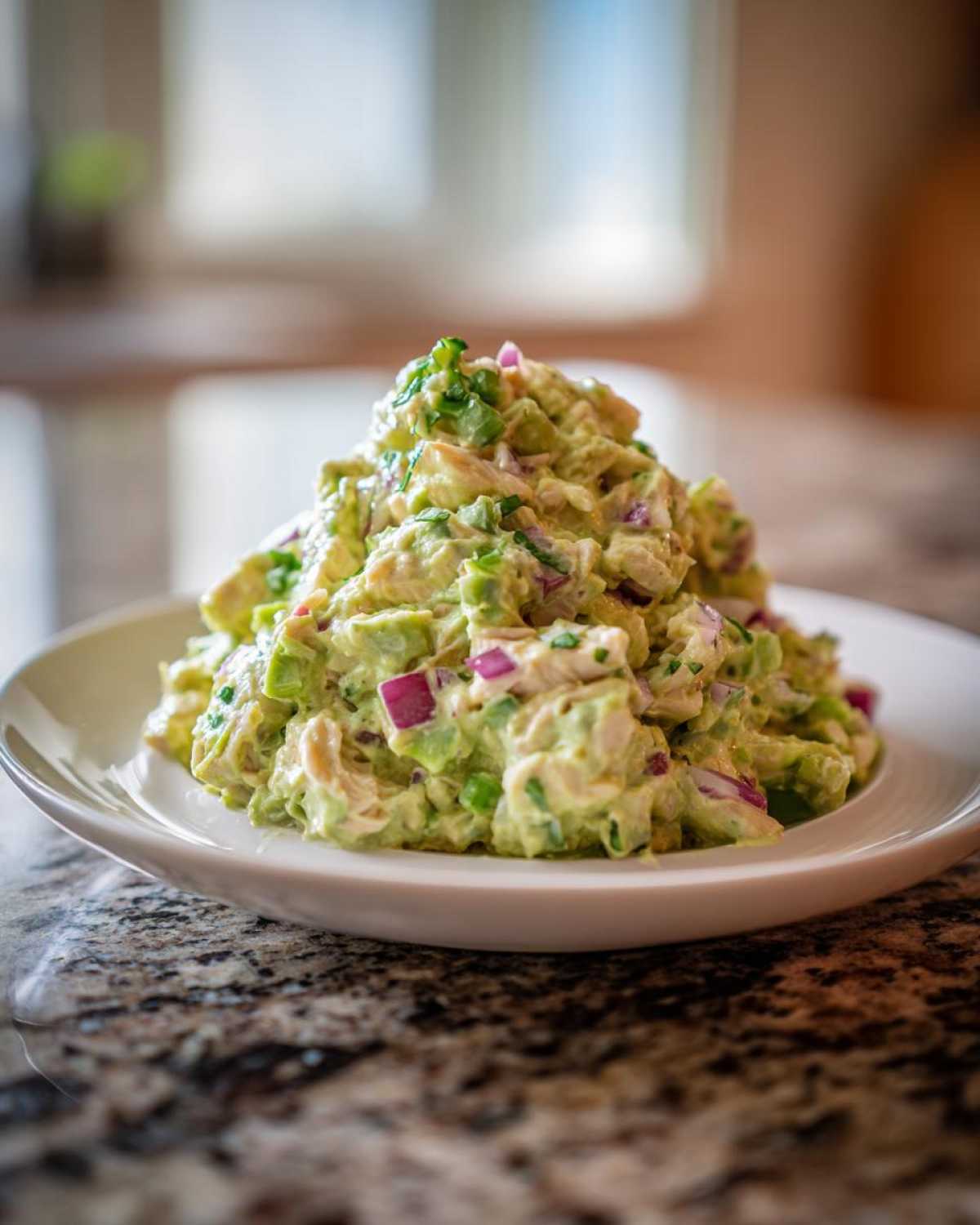 A generous serving of creamy avocado chicken salad mixed with chunks of avocado and red onion on a white plate.