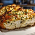 Close-up of a baked caesar chicken breast topped with melted cheese and herbs.