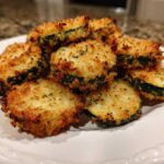 Close-up of golden brown, crispy baked parmesan zucchini slices piled on a white plate.