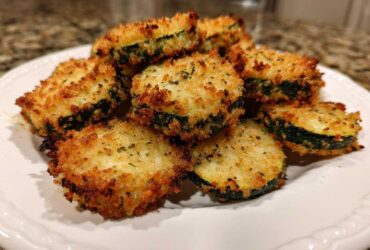 Close-up of golden brown, crispy baked parmesan zucchini slices piled on a white plate.