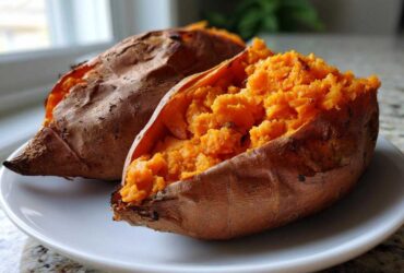 Two perfectly baked sweet potatoes, one split open to show the fluffy, bright orange interior.