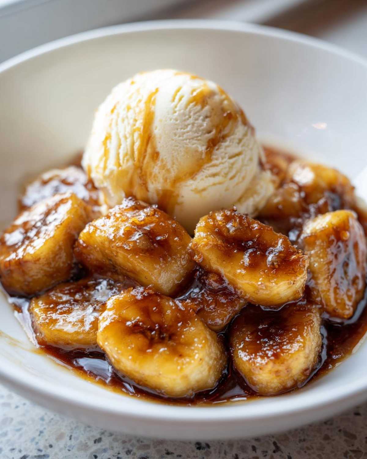Close-up of delicious bananas foster served in a white bowl topped with a scoop of vanilla ice cream.