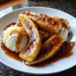 Close-up of warm, caramelized bananas foster served over scoops of vanilla ice cream with rich caramel sauce.