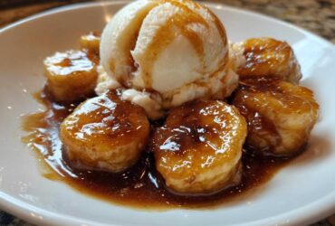 Close-up of caramelized bananas foster slices topped with a scoop of vanilla ice cream and rich sauce.