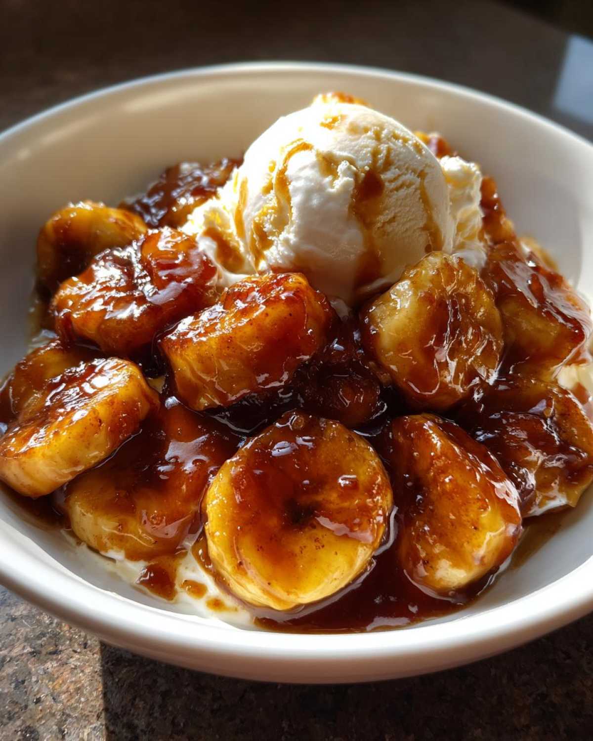 A close-up of warm, caramelized bananas foster served in a white bowl topped with a scoop of melting vanilla ice cream.