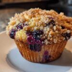 Close-up of a golden blueberry muffin with juicy berries and a generous streusel crumb topping.