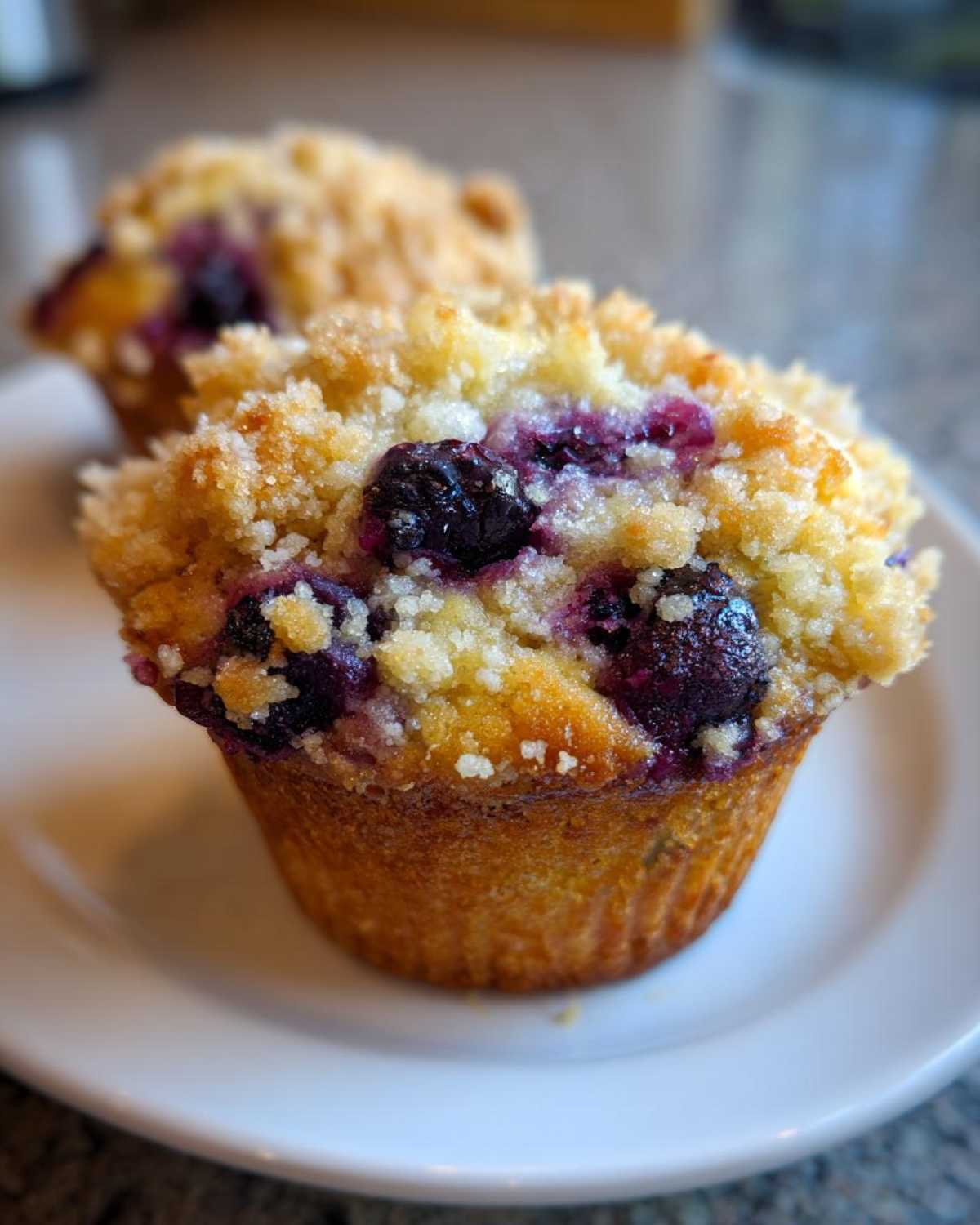 A close-up of a golden brown blueberry muffin topped with sweet streusel crumb, featuring visible plump blueberries.