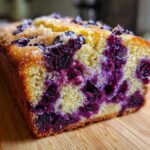 A close-up, cross-section view of a moist blueberry banana bread loaf studded with deep purple blueberries.