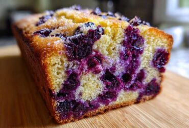 A close-up, cross-section view of a moist blueberry banana bread loaf studded with deep purple blueberries.
