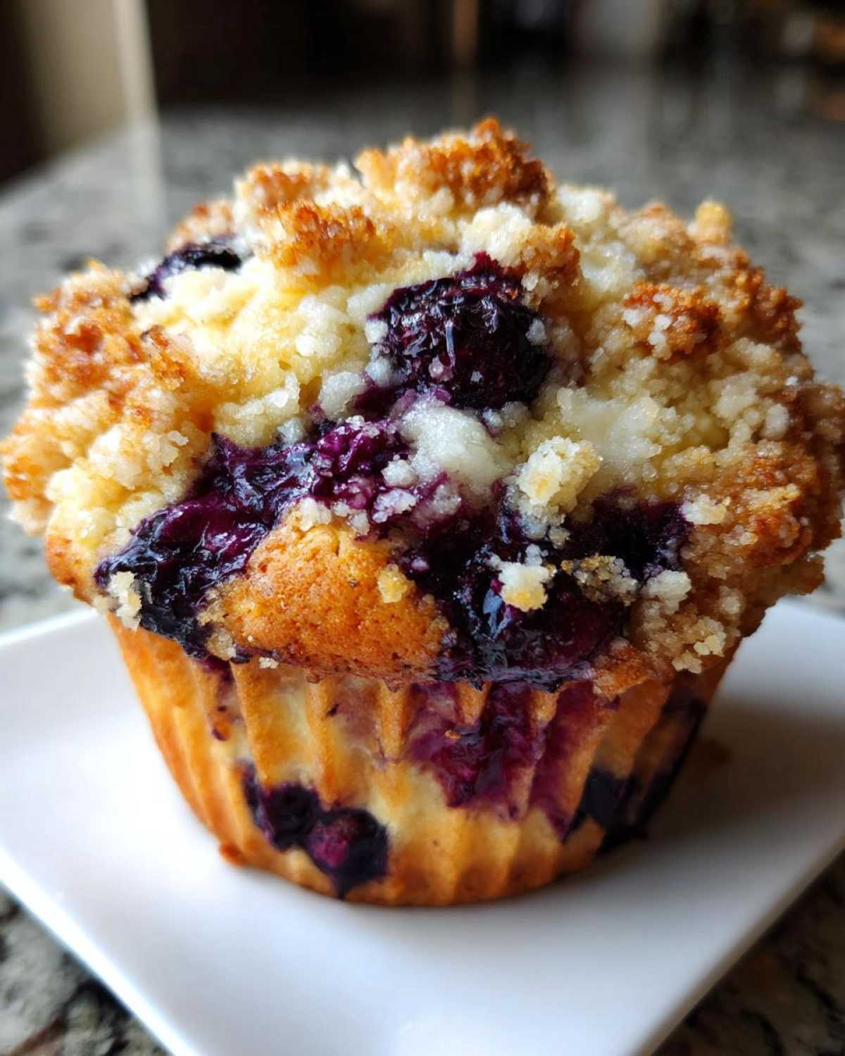 Close-up of a golden brown blueberry muffin topped with sweet streusel crumbs and bursting blueberries.