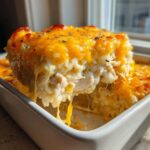 A scoop of creamy cheesy chicken and rice casserole being lifted from a white dish, showing melted, stretchy cheese.