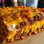 A thick, cheesy slice of Dorito Casserole showing layers of seasoned ground beef, melted cheddar, and crushed chips.