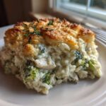 A square serving of creamy chicken broccoli rice casserole with a golden, crispy topping on a white plate.