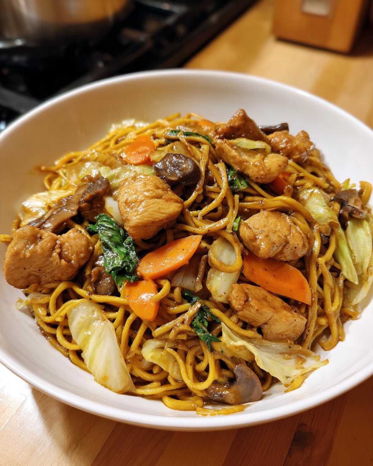 A close-up of a generous serving of chicken chow mein recipe with noodles, chicken pieces, carrots, and cabbage.
