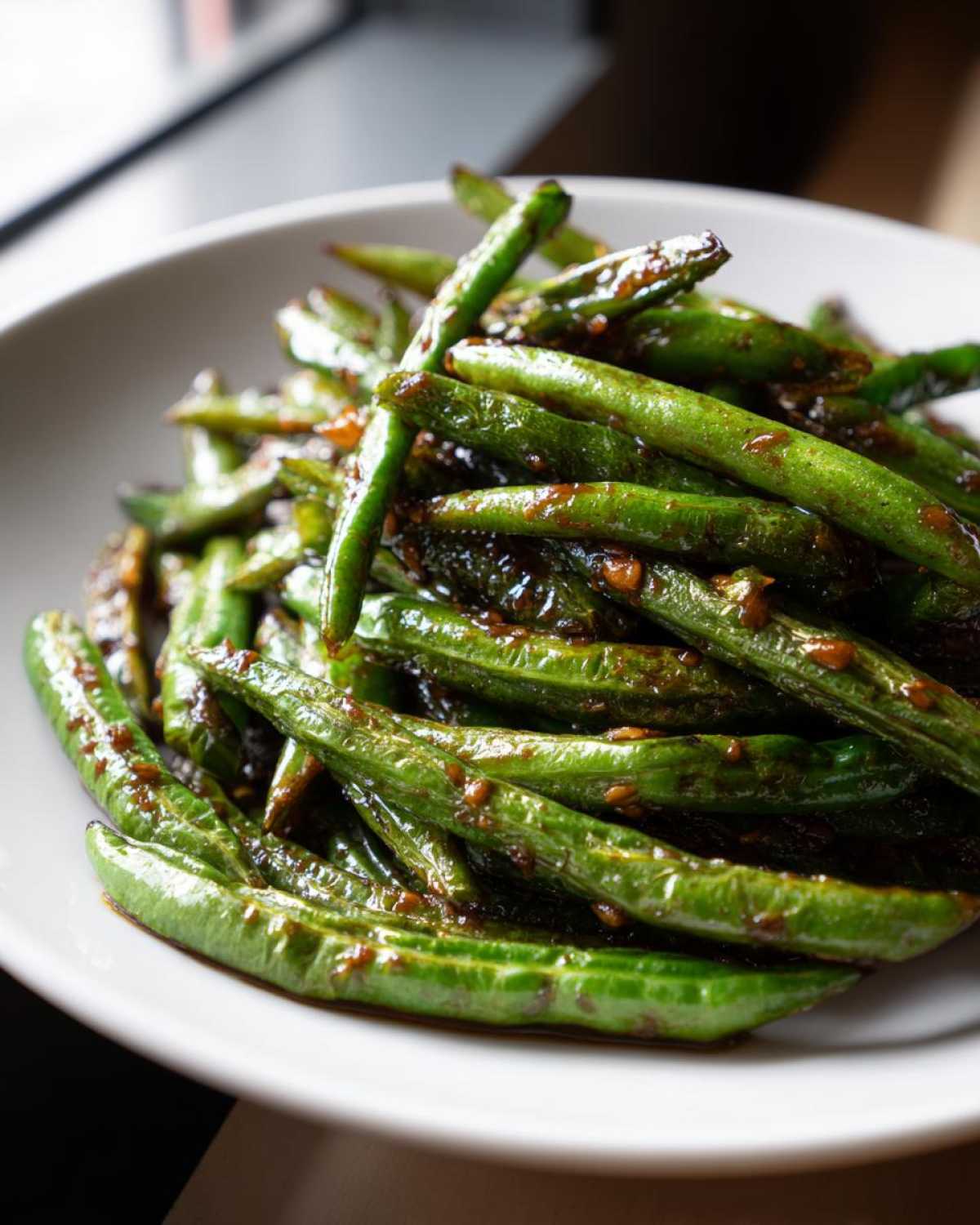 Close-up of vibrant green beans coated in a rich, glossy garlic sauce, ready to serve.