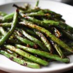 A close-up serving of vibrant green beans coated in a glossy, dark garlic sauce, ready to eat.