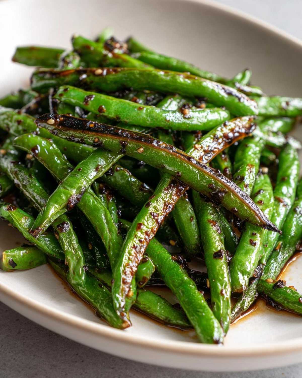 A close-up of vibrant, blistered Chinese green beans with garlic sauce and sesame seeds served in a light bowl.